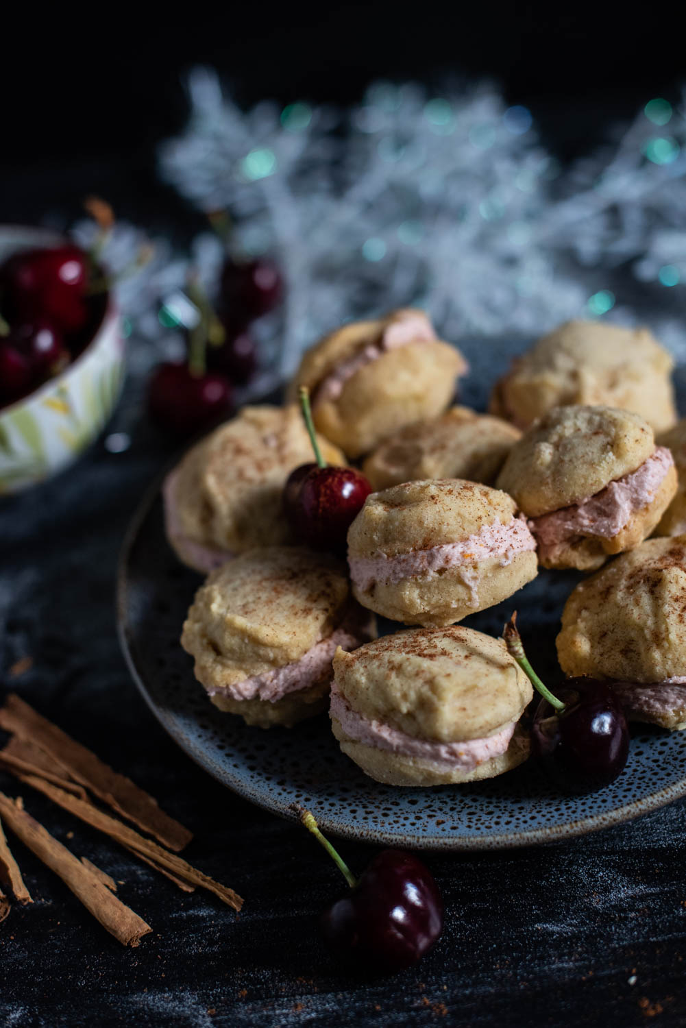 Cinnamon shortbread cookies with a creamy cherry filling surrounded by cherries on a plate with moody lighting