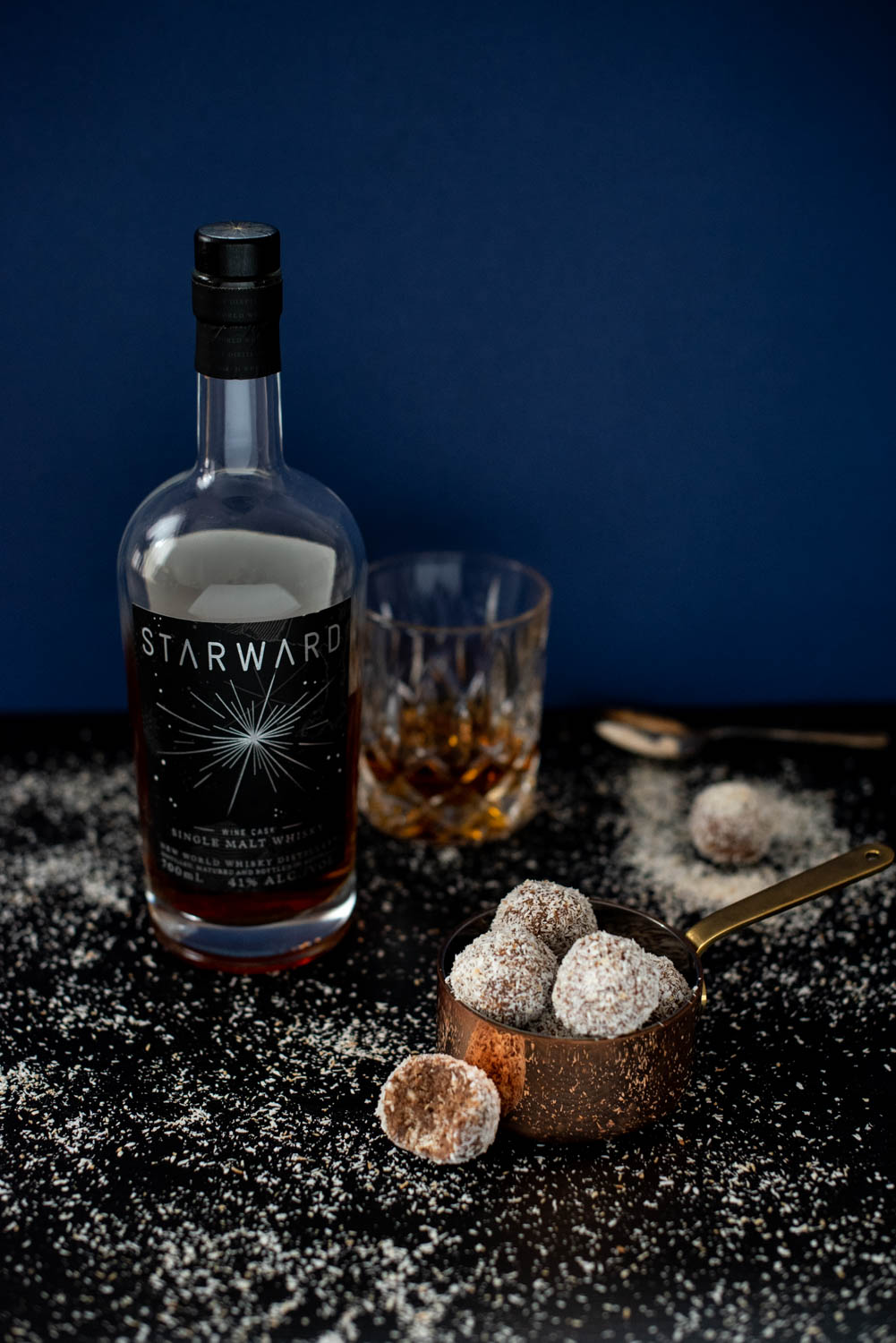 Whisky balls covered in toasted coconut with a Riddle glass holding whisky and a bottle of Starward wine cask whisky in the background