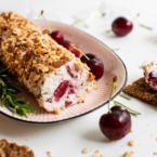 A cheese log made with cream cheese, feta and cherries and coated in toasted almonds on a plate with crackers